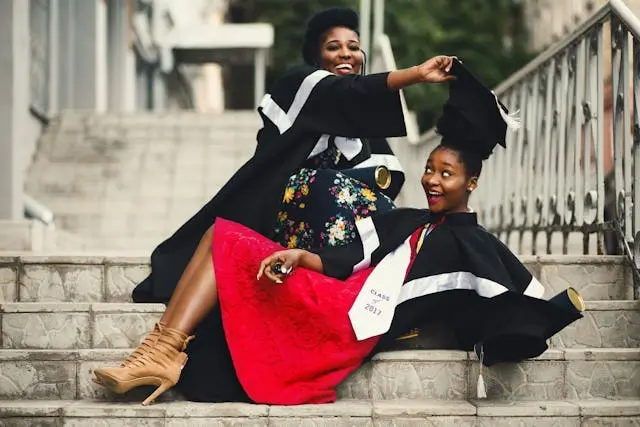 Two women in graduation robes lounging on outdoor stairs