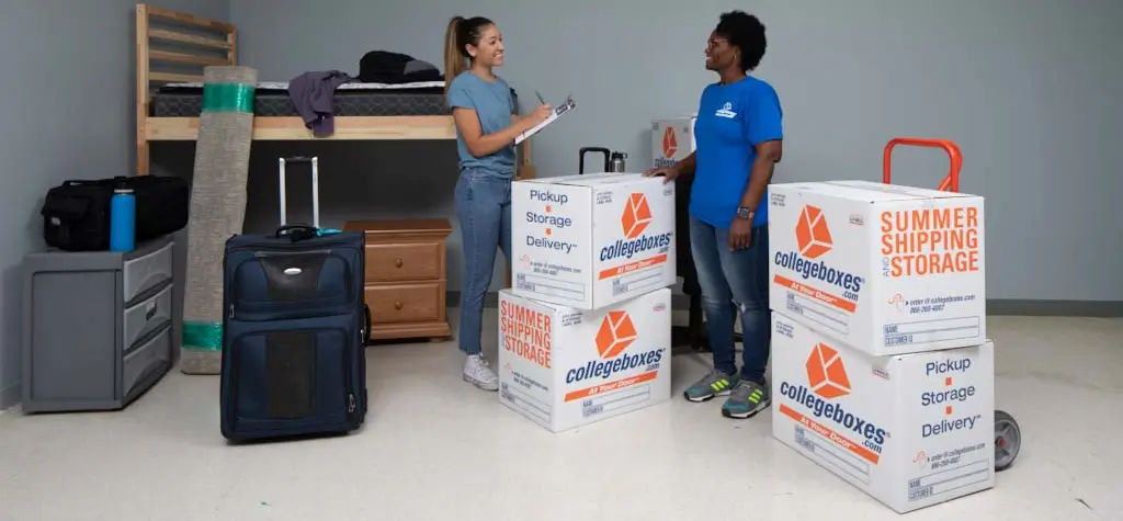 Two women standing in an empty dorm with boxes and luggage