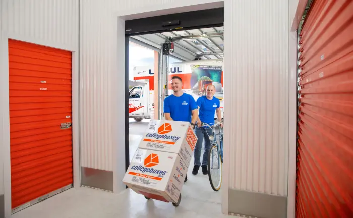 Two people loading Collegeboxes branded boxes and a bike into a storage unit facility