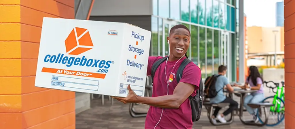 Young man outside holding a Collegeboxes box